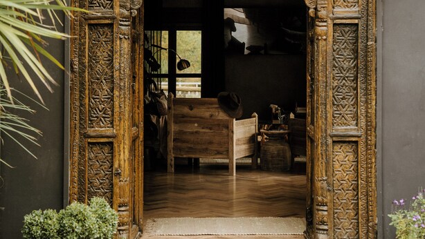 Una entrada ornamentada con intrincados grabados, una puerta de madera y un pequeño jardín con una jaula de pájaros y plantas en macetas.