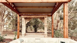 Un jacuzzi bajo una pérgola de madera con vista a árboles.
