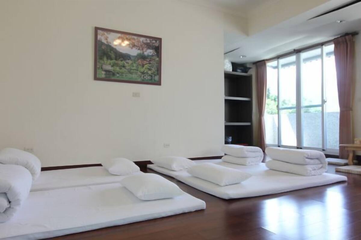 A room with two massage tables, a painting on the wall, and a large window with curtains.