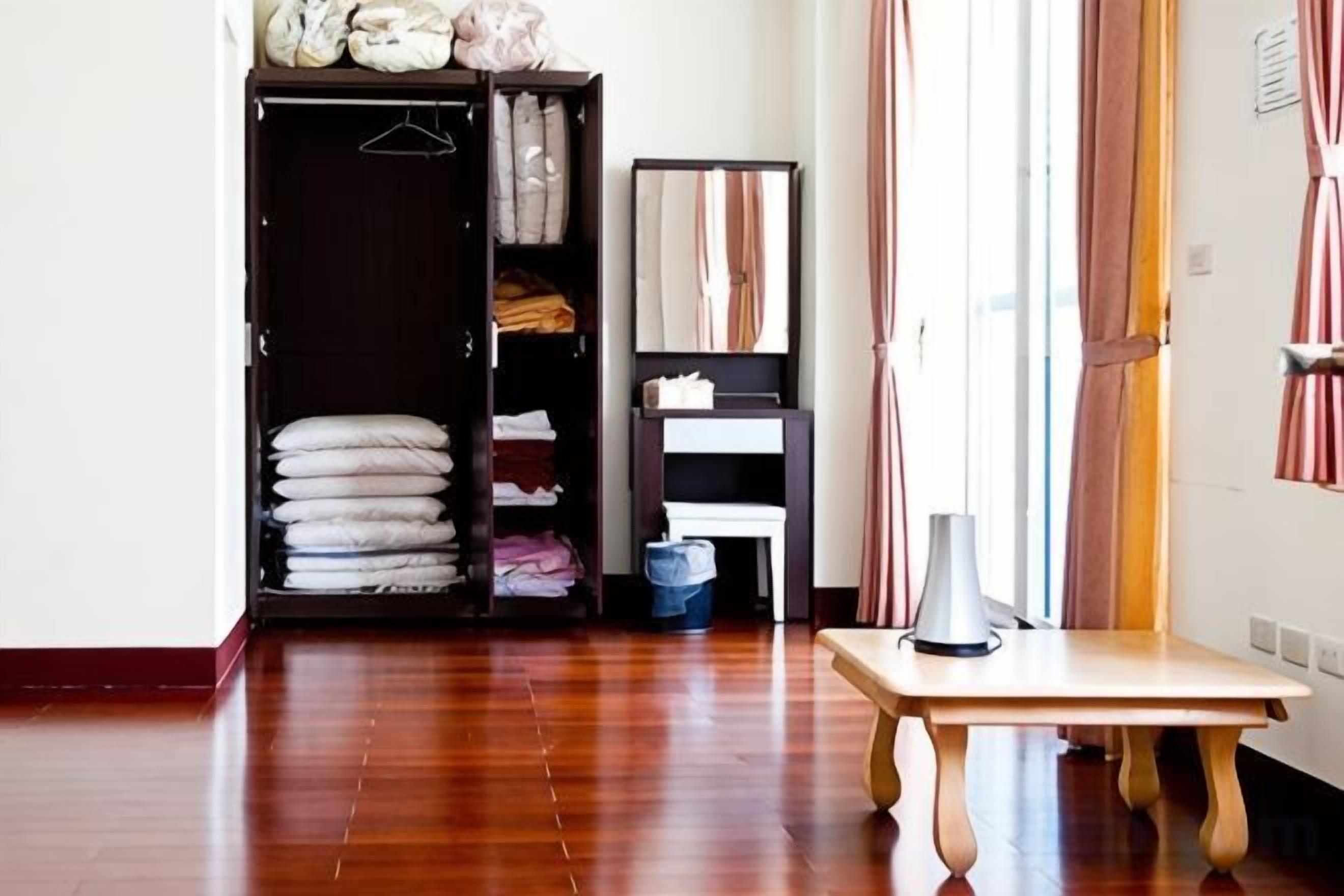 A room with a wooden floor, a table, a wardrobe, and a window with curtains.