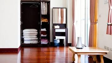A room with a wooden floor, a table, a wardrobe, and a window with curtains.