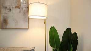 A room with a floor lamp, a painting, and a plant.