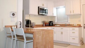 A compact kitchen with white cabinets, a microwave, a coffee maker, and a small dining area with two chairs.