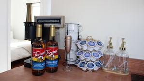 A hotel room with a bed, a coffee station, Torani vanilla bean syrup, and Torani coffee mugs.