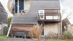 A two-story house with a grey tiled roof, a wooden garage door, and a small garden area with gravel paths and plants. - Holiday Home in Yn e Lijte With Water Sports (Grou)