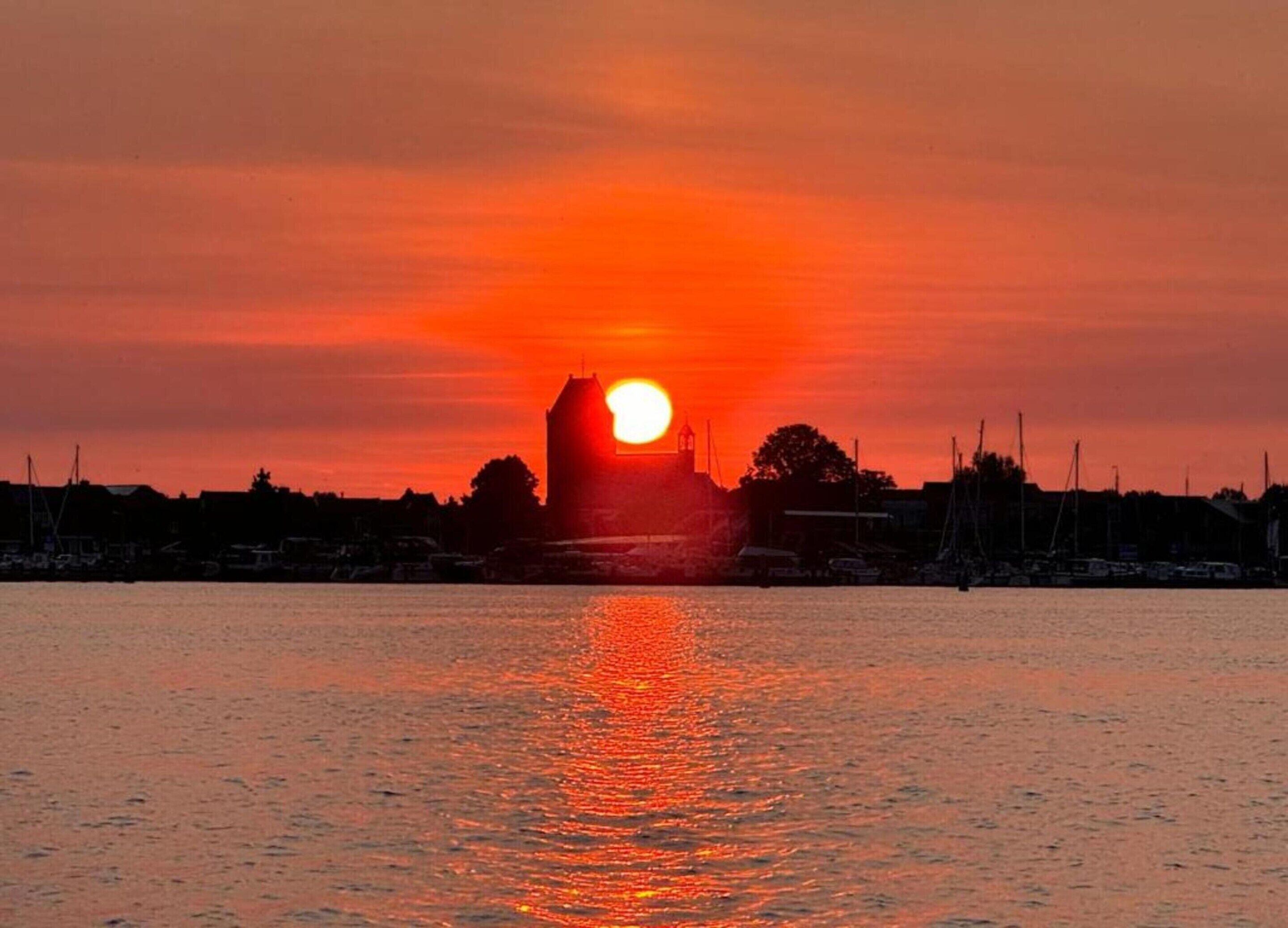 A sunset over a harbor with boats and a prominent building silhouetted against the sky.