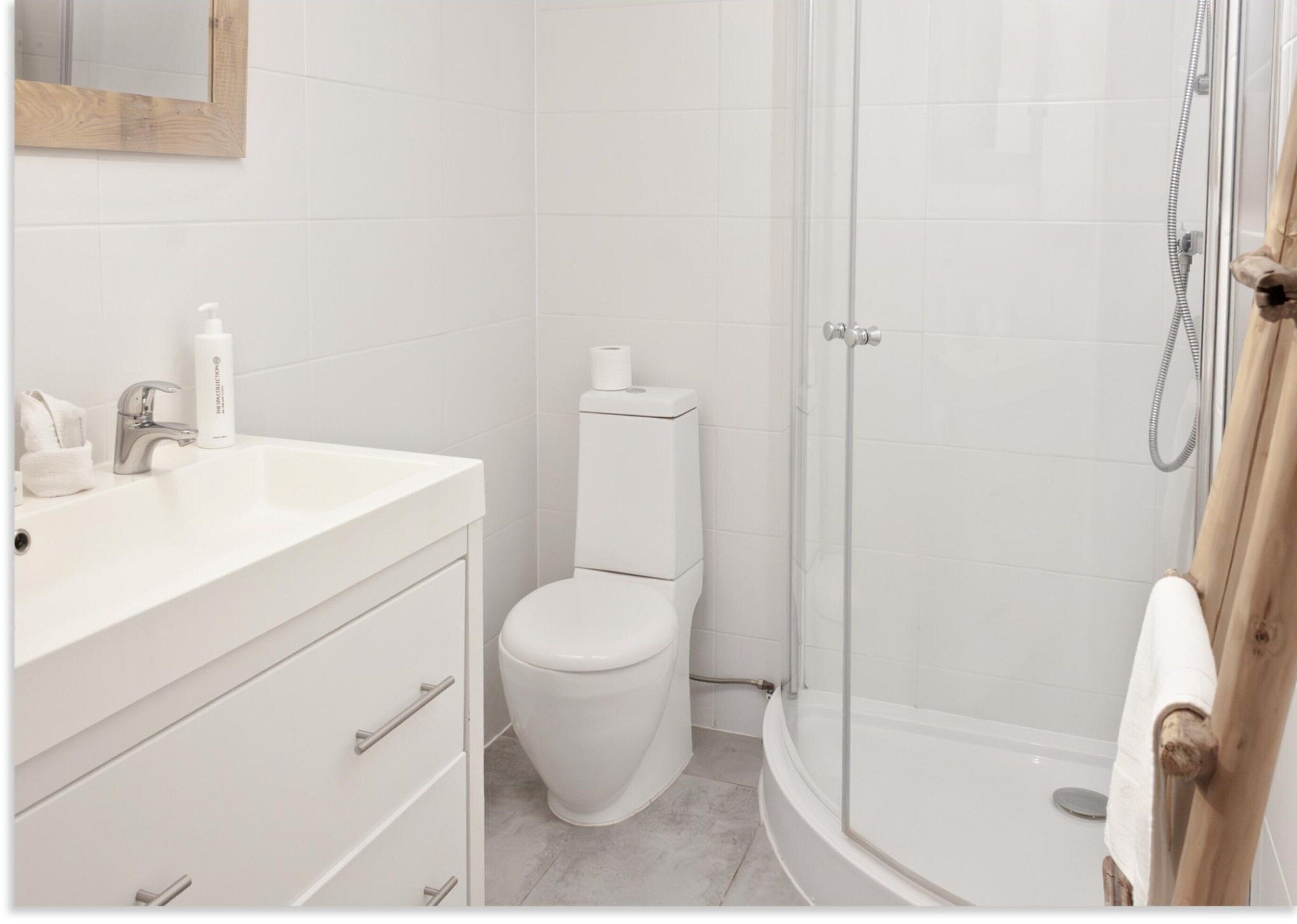 Casa de banho moderna com lavatório, sanita e chuveiro, tudo em branco.