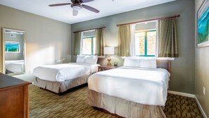 A hotel room with two beds, a ceiling fan, a window with curtains, and a wooden floor.