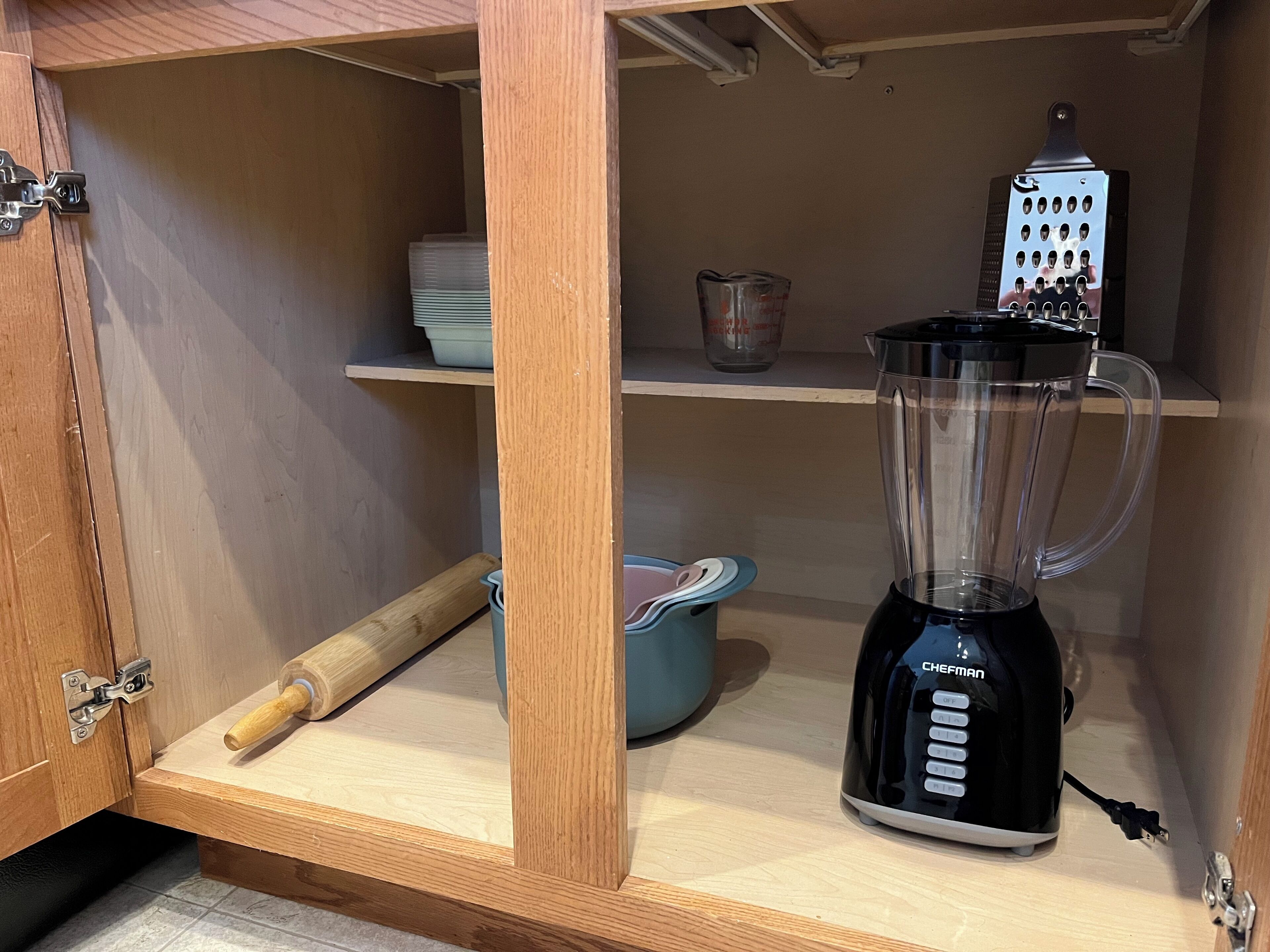Una cocina con un armario de madera, una licuadora, un rallador y un rodillo sobre la encimera.