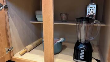 Una cocina con un armario de madera, una licuadora, un rallador y un rodillo sobre la encimera.