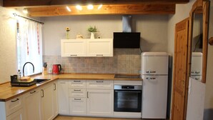 Une cuisine avec des armoires blanches, un plan de travail en bois, un four encastré et un réfrigérateur.