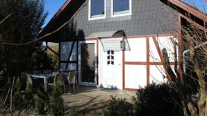 Une maison à deux étages, avec un toit gris, des boiseries blanches et un petit porche à l’avant, agrémenté d’une table et de chaises.