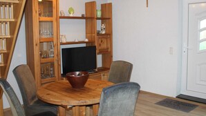 A dining area with a wooden table and chairs, a television, and built-in wooden shelving with glassware. - Ferienhaus in Rethwisch (Boergerende-Rethwisch)