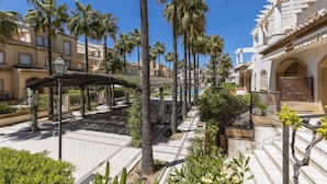 Une cour intérieure agrémentée de palmiers, d’une pergola et d’un espace piscine.
