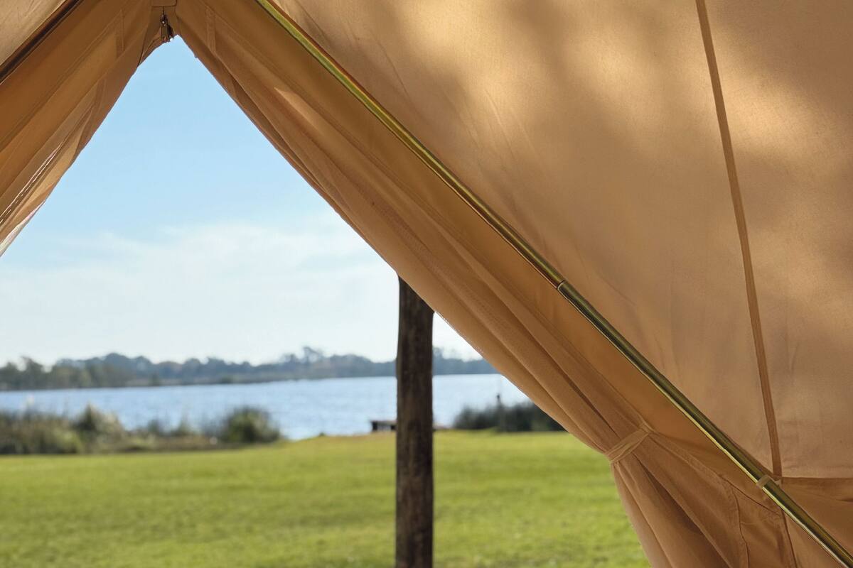 A tent with a view of a lake and grassy field.