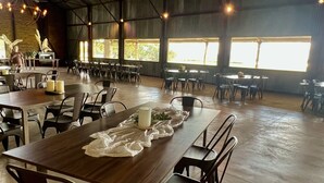 Un amplio comedor interior con varias mesas y sillas, ventanas grandes que dejan entrar luz natural y un ventilador de techo.