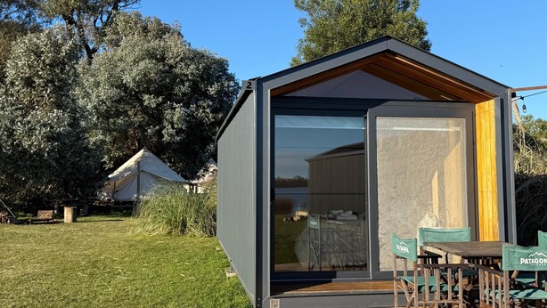 Un edificio moderno y compacto con puerta de vidrio, terraza de madera y asientos al aire libre.