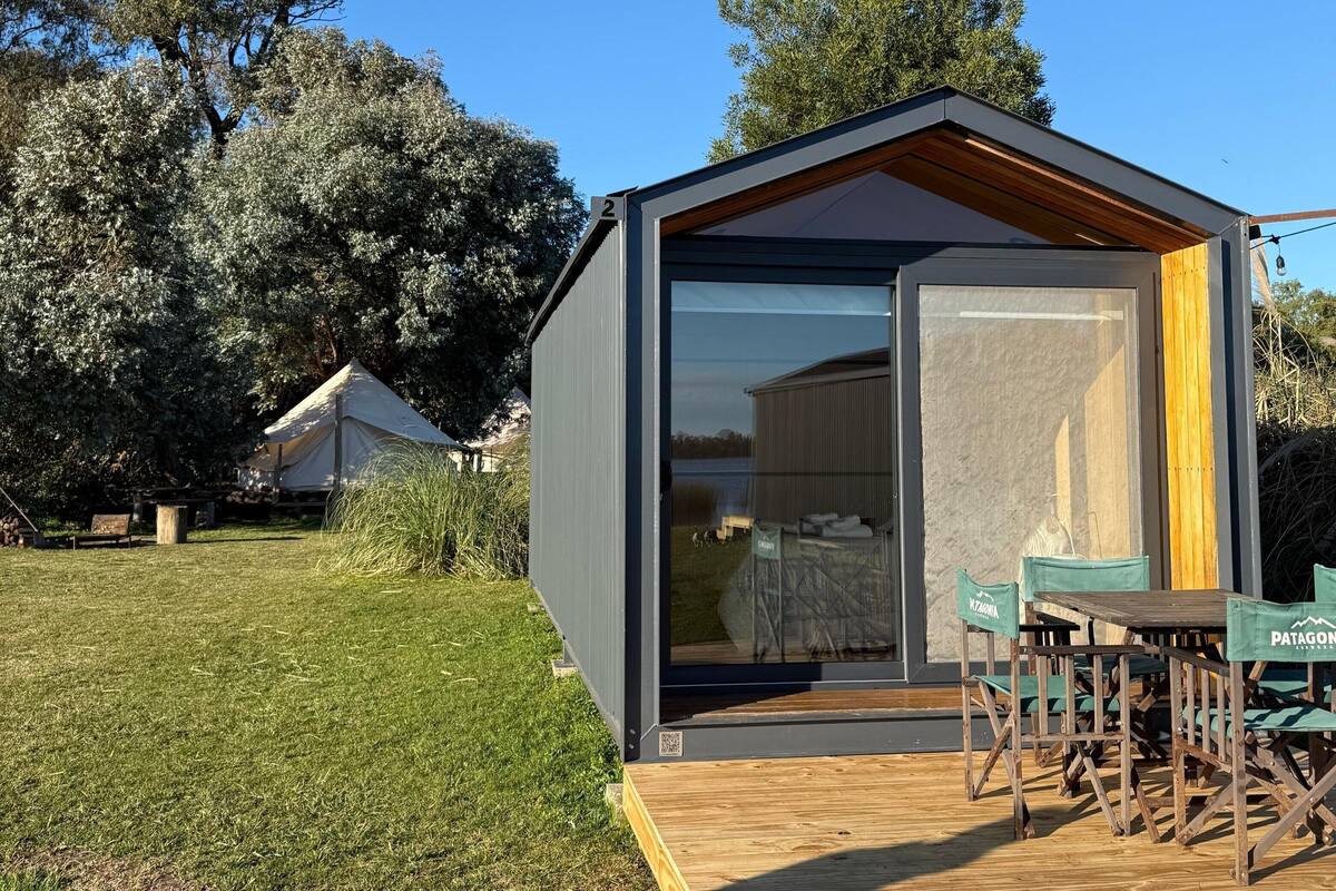 A modern, compact building with a glass door, a wooden deck, and outdoor seating.