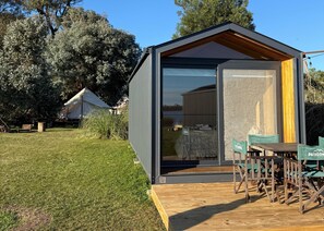 Un edificio moderno y compacto con puerta de vidrio, terraza de madera y asientos al aire libre.