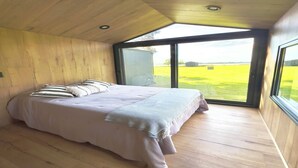 Un dormitorio con una cama grande, paredes de madera y un ventanal con vistas a un campo verde.