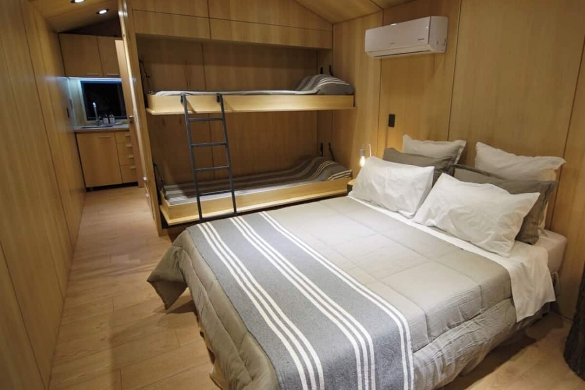 A compact room with bunk beds, a small kitchenette, and a bedside table with a lamp.