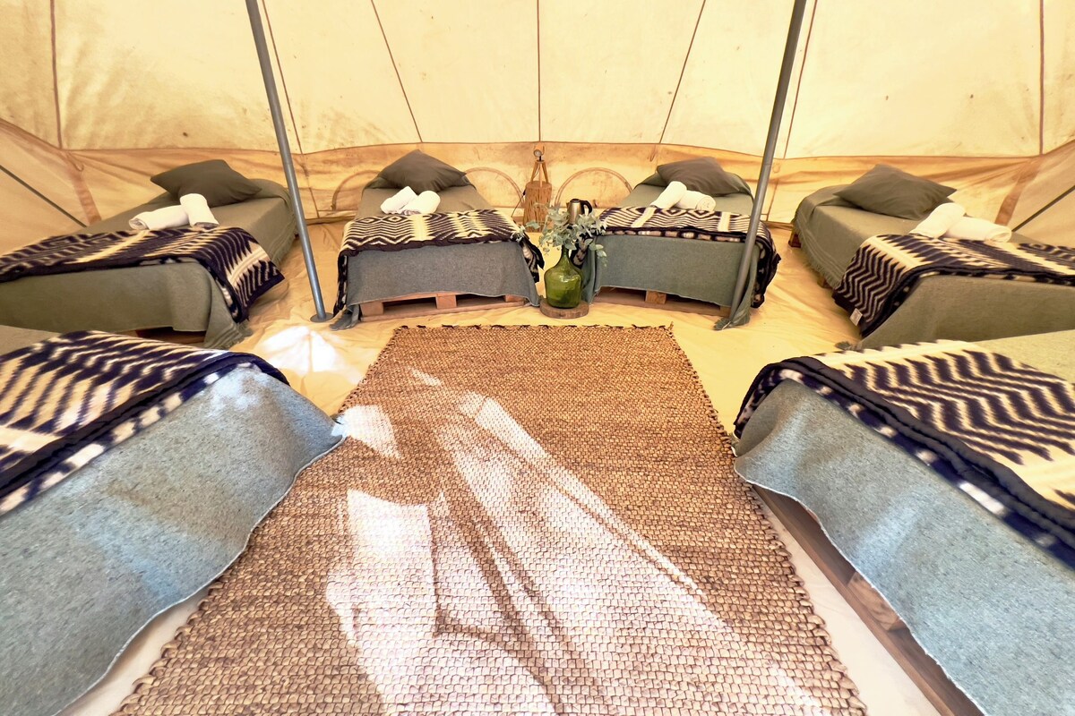 A tent with four beds, each with a patterned blanket and pillows. A woven mat is placed in the center.