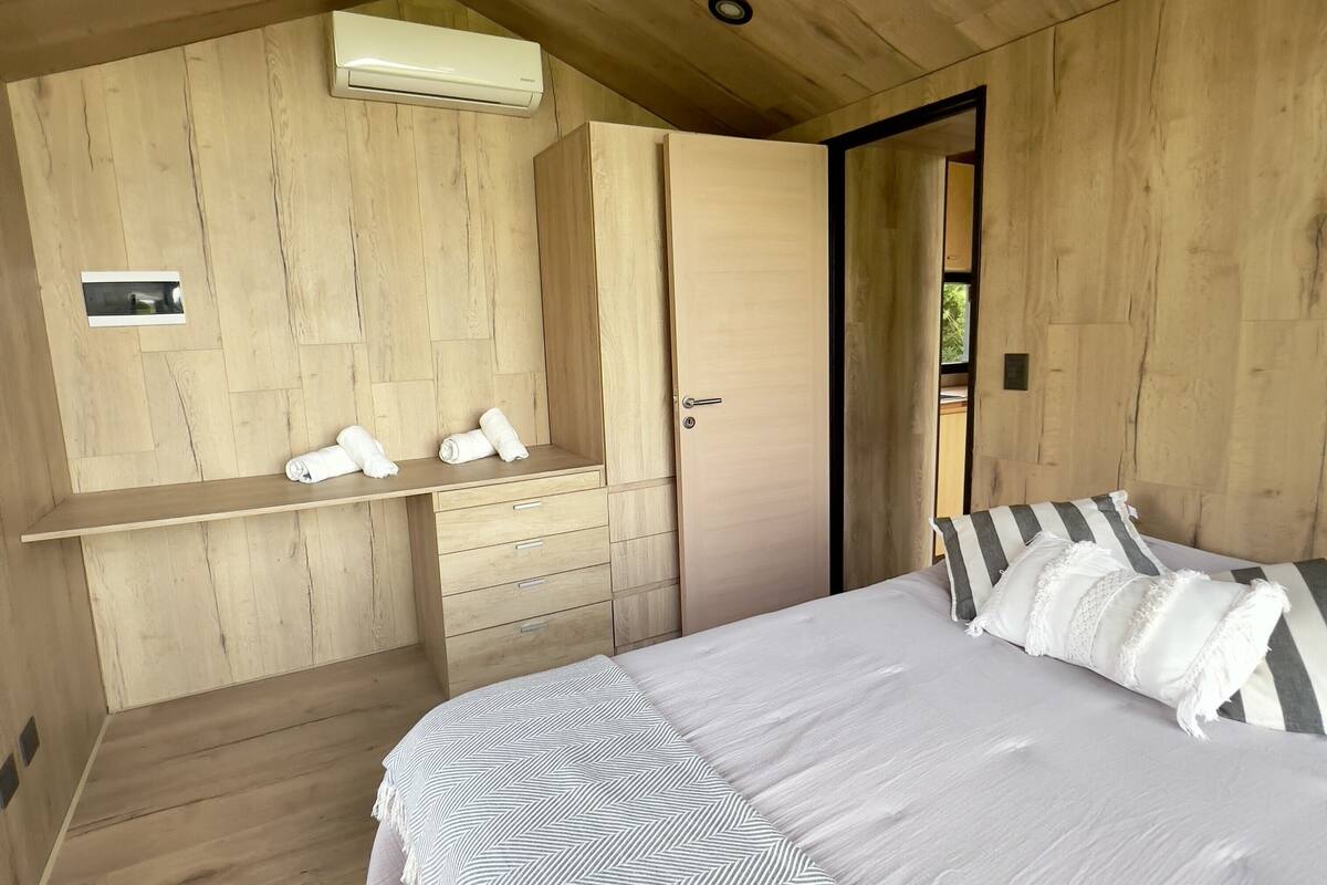 A wooden room with a bed, a wardrobe, and a shelf with towels.