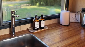 Una cocina con un lavamanos de acero inoxidable, dos botellas de vino Lavamanos y un rollo de toallas de papel sobre una encimera de madera.