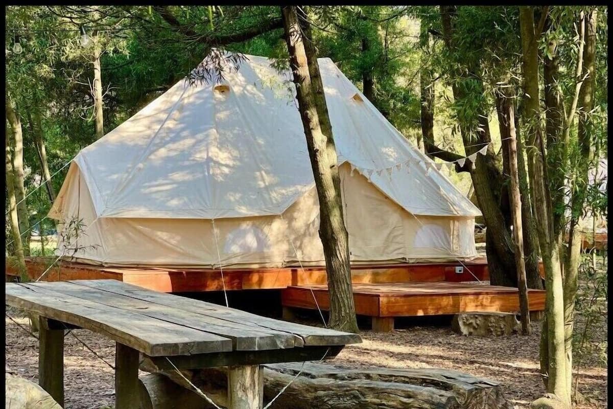 A tent with a wooden platform and a picnic table in a forest setting.