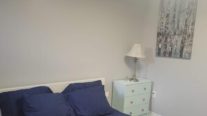 Ein Schlafzimmer mit einem Bett, einem Nachttisch mit Lampe und einem an der Wand hängenden Kunstwerk.