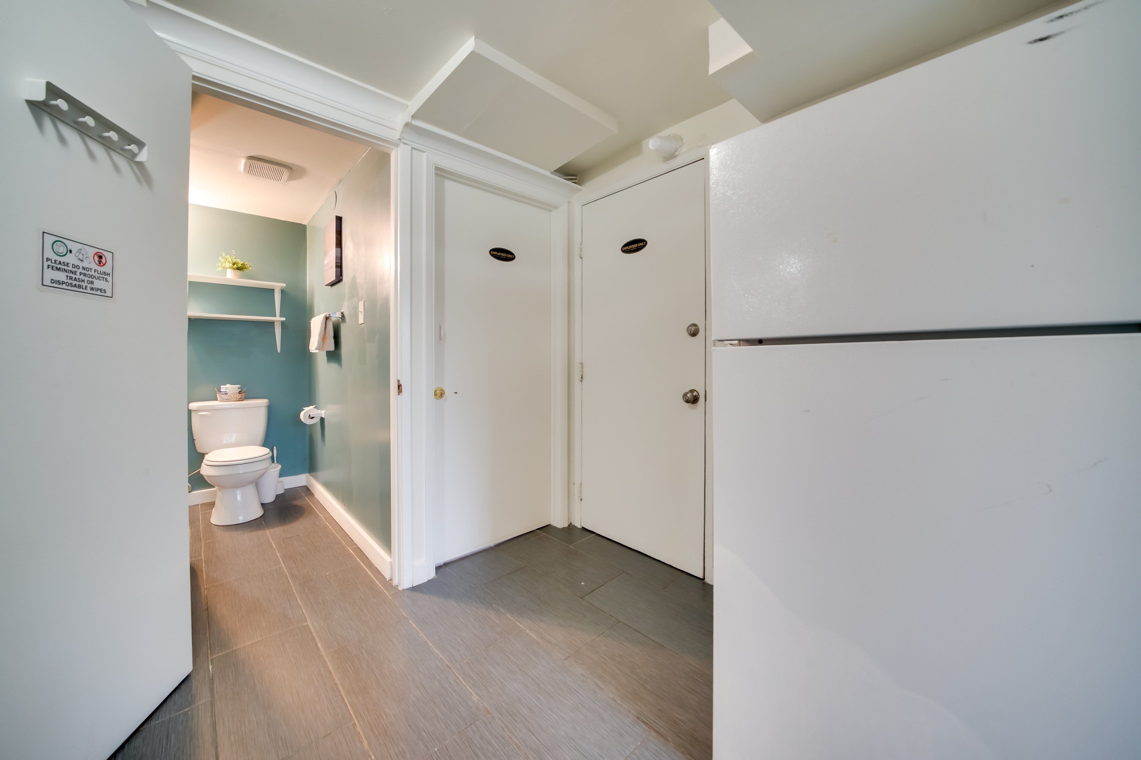 Un baño con inodoro, una repisa con una planta y una puerta con un letrero.