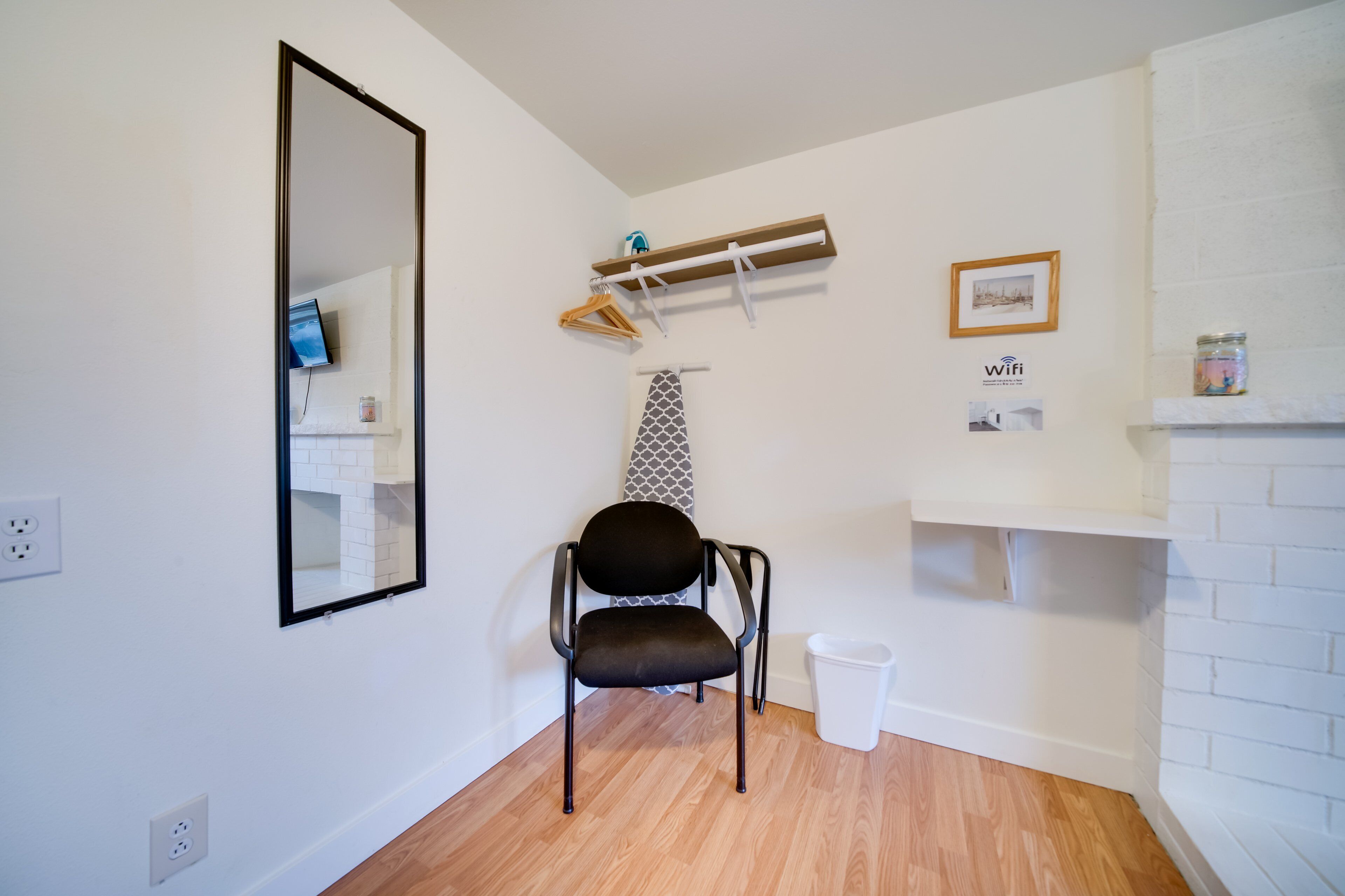 Une salle de bain avec un miroir, une chaise noire, un porte-serviettes, une étagère avec un pot et un panneau indiquant la présence d’une connexion Wi-Fi.
