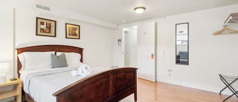 Une chambre à coucher avec un lit en bois, des murs blancs et une porte qui donne sur une autre pièce.