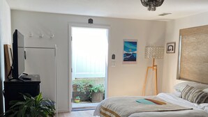 Ein Schlafzimmer mit Bett, Schreibtisch, Stuhl, einer Zimmerpflanze, einem Teppich, einem Bild und einem Fenster.