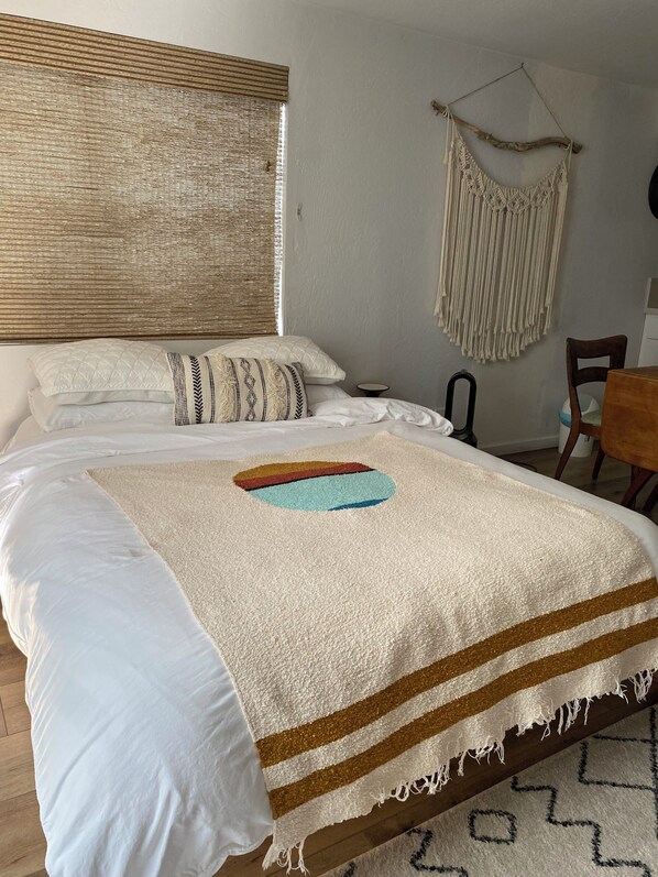 A neatly made bed with a quilted headboard, a hanging macrame wall decoration, and a wooden floor. - Coastal Getaway at Beach Studio With Private Entrance- Includes Parking Spot (Oxnard)