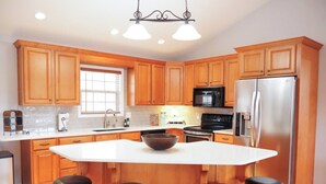 A modern kitchen with wooden cabinets, a central island with stools, stainless steel appliances, and pendant lighting. - Serene Waterfront Lake Wedowee Home (Wedowee)