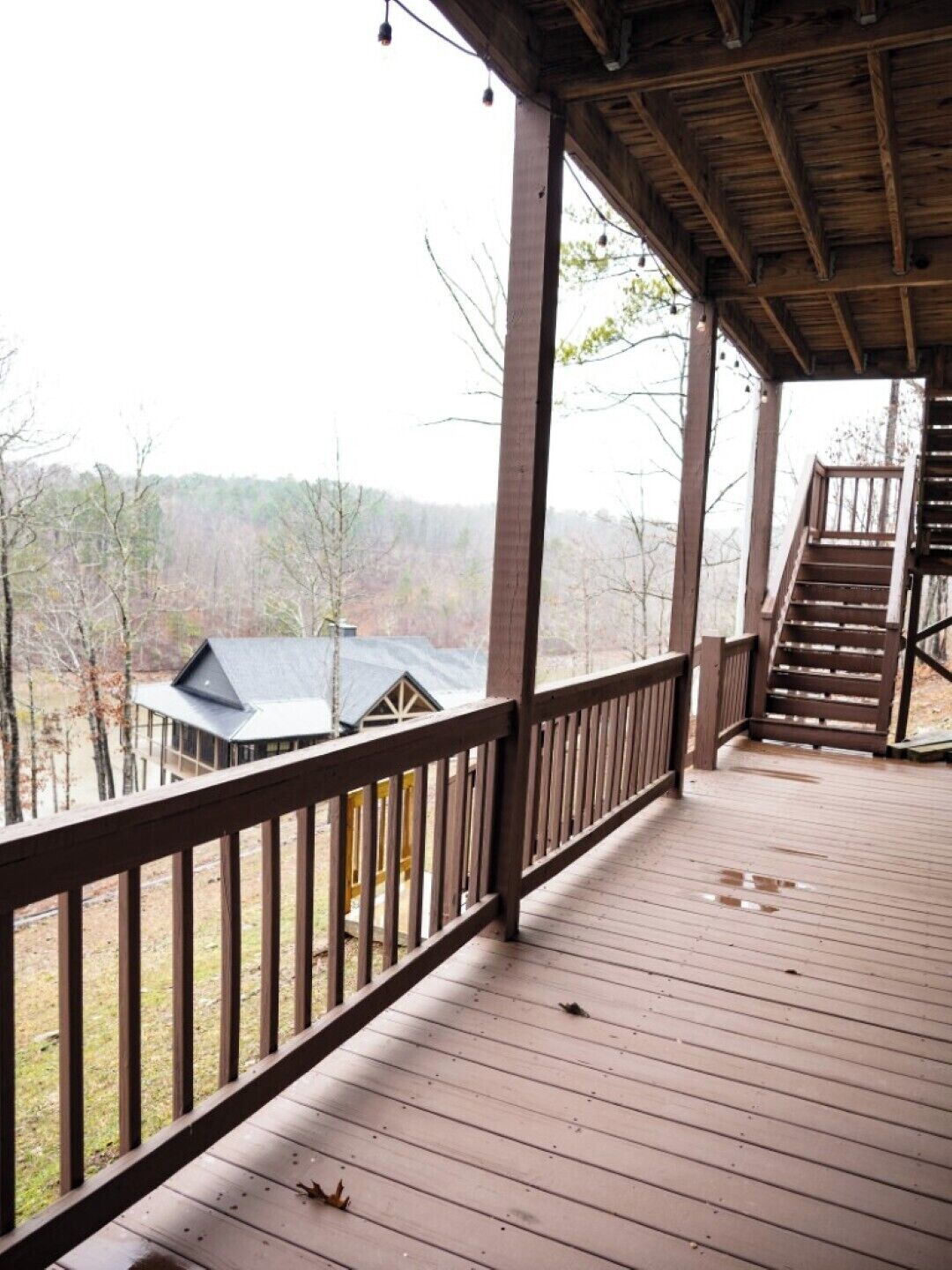 A wooden deck with a railing, a staircase, and a view of a house and trees.