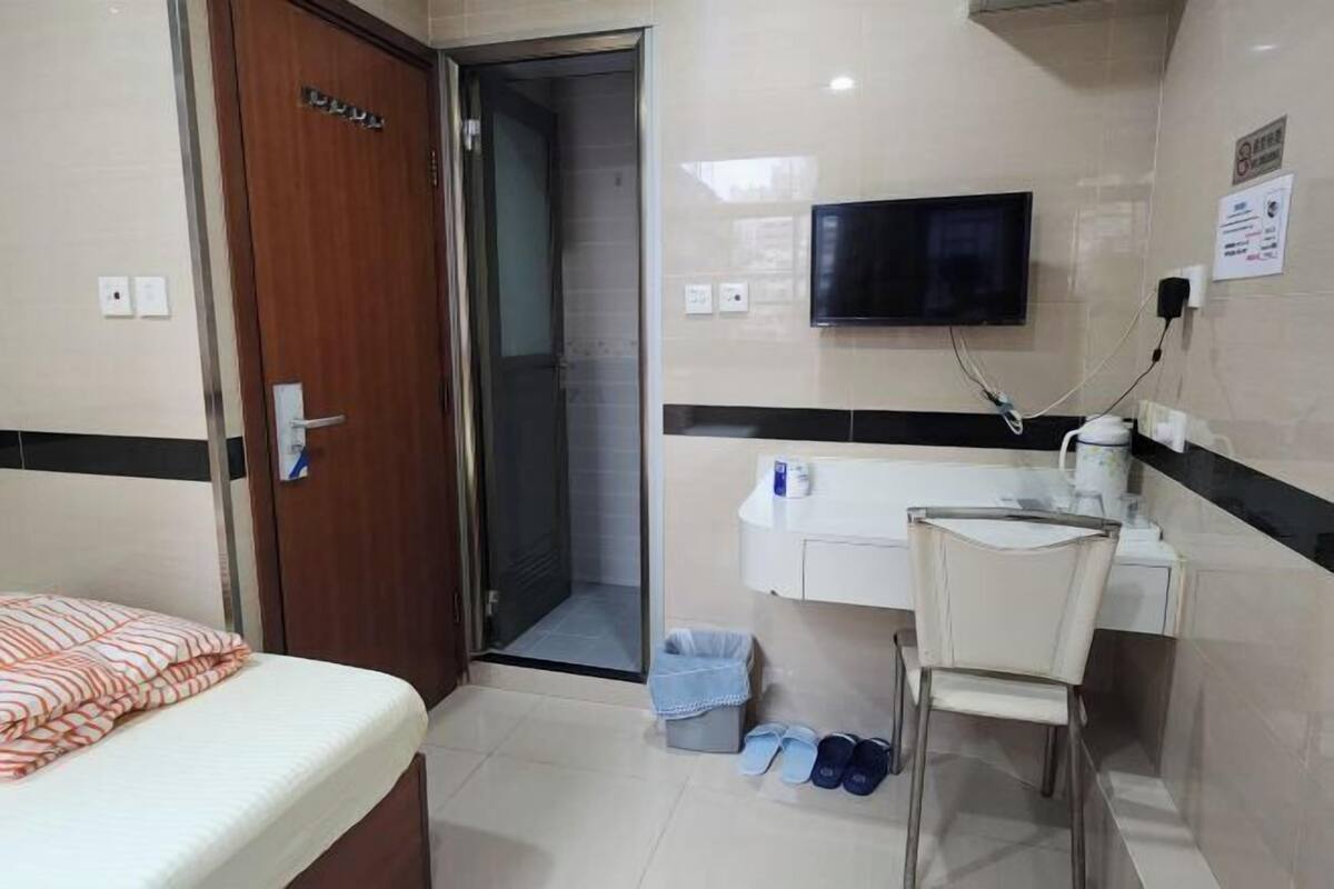 A hotel room with a bed, a TV, a small desk with a chair, and a trash bin.