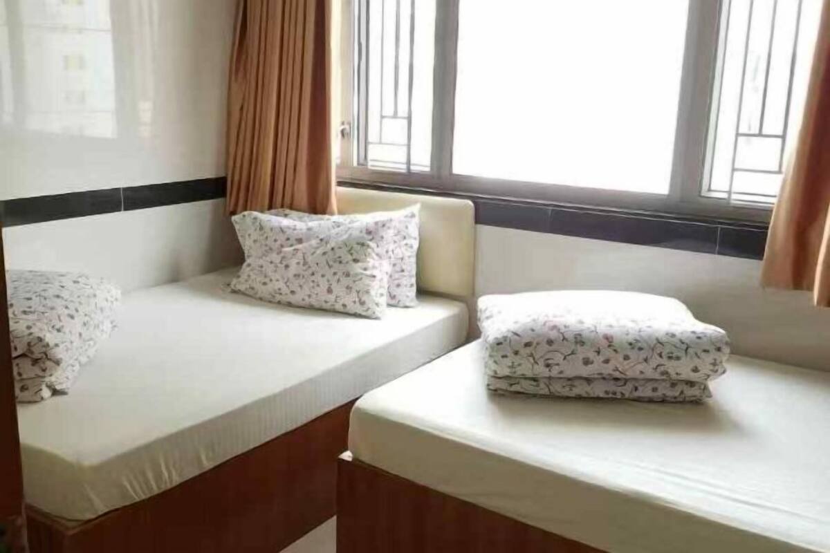A hotel room with two single beds, a window with curtains, and a view of the outside.