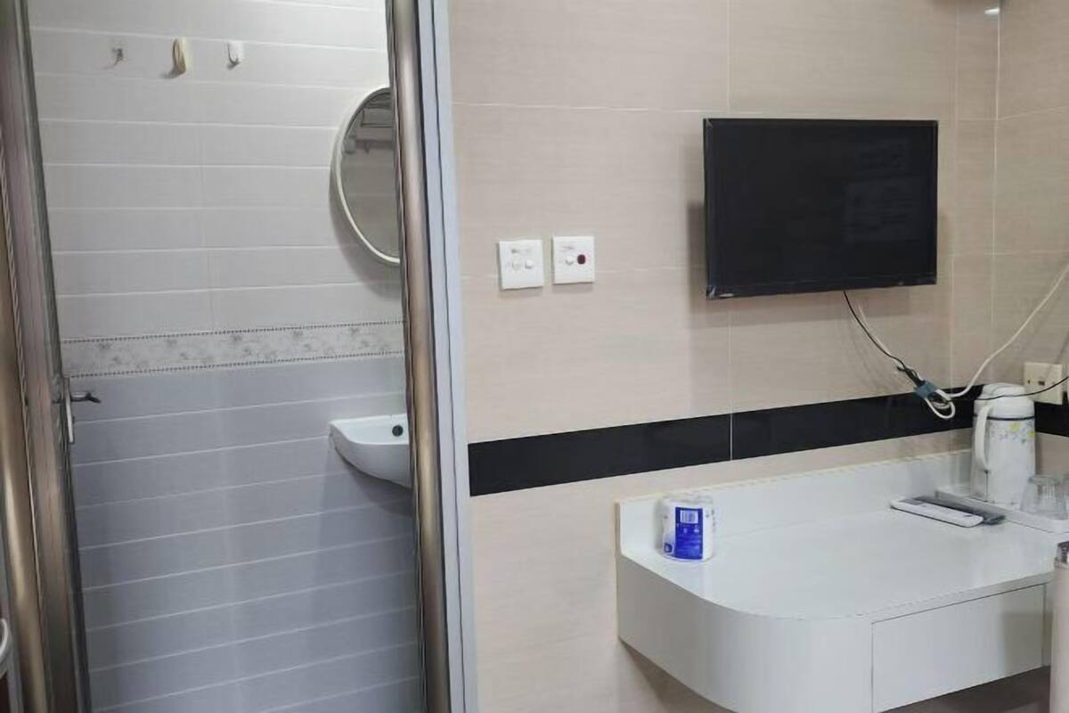 A bathroom with a toilet, a sink, a mirror, and a television mounted on the wall.