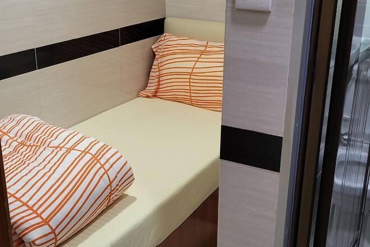 A single bed with striped bedding, a headboard with black and white paneling, and a wall-mounted air conditioning unit.