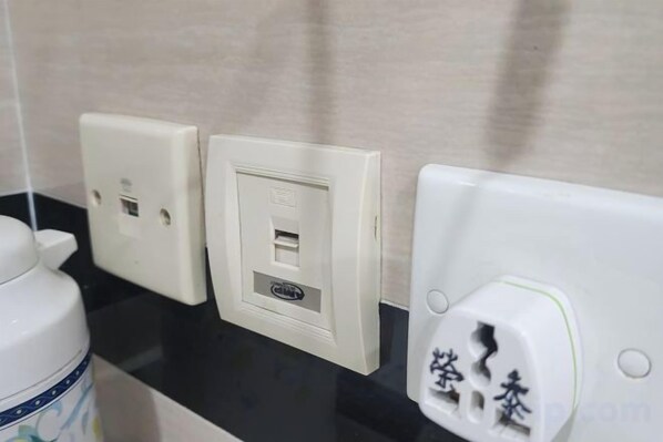 A bathroom with a black countertop, a white wall socket with a USB port, and a white electrical outlet with a plug. - Wing Tai Guest House (Hong Kong)
