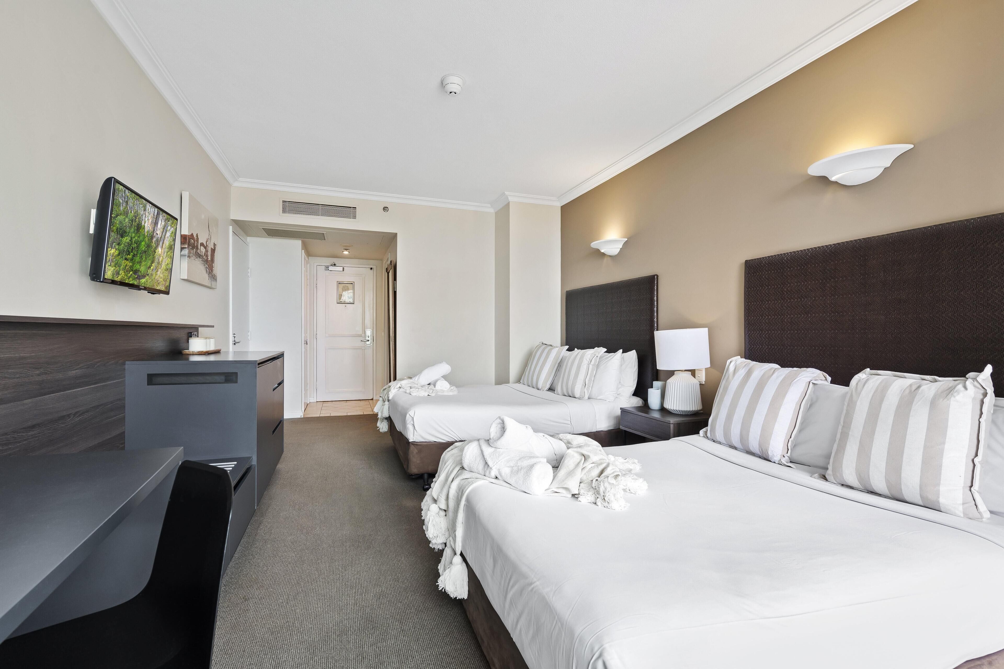 A hotel room with two beds, a desk, a TV, and a bathroom door.
