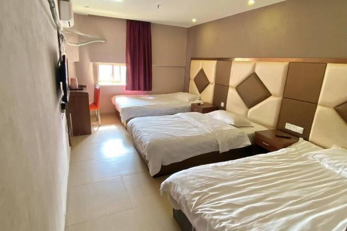 A hotel room with two beds, a TV, a desk, and a window with curtains.