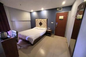 A hotel room with a bed, a desk with a chair, a door, and a small table with a kettle. - Shanghai Longting Hotel (Shanghai)
