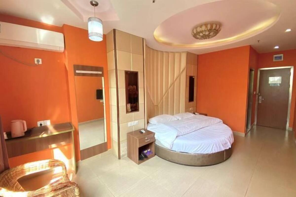 A hotel room with a round bed, a small bedside table, a mirror, and a wall-mounted air conditioning unit.