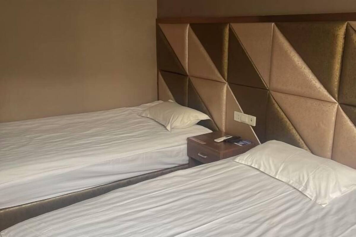 A hotel room with two single beds, a wooden nightstand, and a headboard with a geometric pattern.