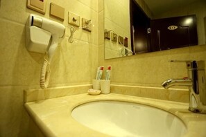 Casa de banho com lavatório, espelho, secador de cabelo e produtos de higiene.
