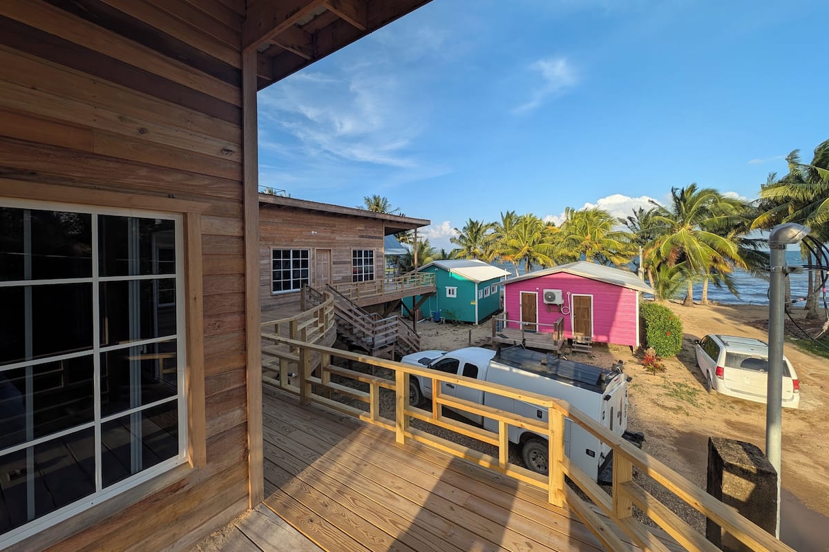 A wooden deck with a view of colorful cabins and a vehicle parked nearby.