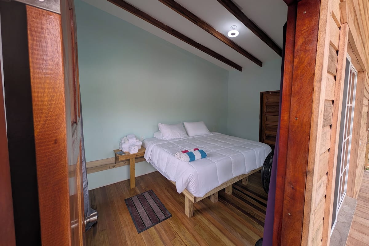 A bedroom with a wooden bed frame, white bedding, and a small bedside table with towels.